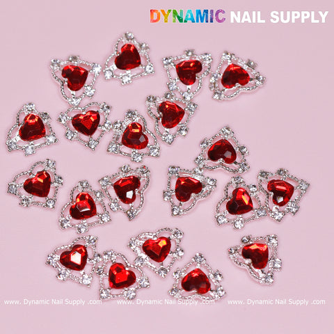 An arrangement of 20 intricately designed 3D Heart rhinestone charms for Nail Art Design is set against a pink background, each featuring red stones encircled by small clear rhinestones. The charms are crafted with a sparkling silver claws base. In the top right corner, the text "Dynamic Nail Supply" is prominently displayed, making it an ideal choice for nail art enthusiasts.