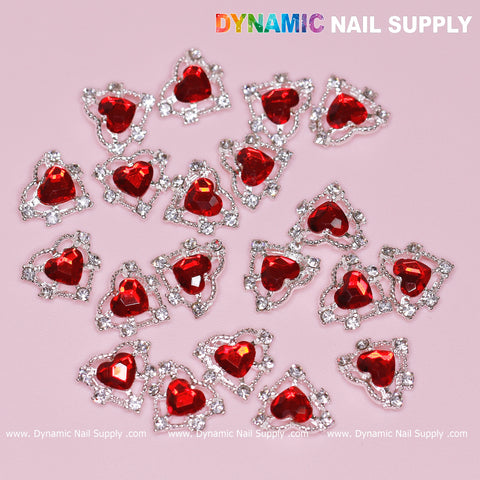 The image features the elegant 20-piece set of 3D Heart Rhinestone Charms for Nail Art Design, with red stones secured in silver claw bases, against a soft pink background. Symbolizing sophistication, Dynamic Nail Supply's logo is prominently displayed at the top right corner, and their website URL is stylishly located at the bottom edge. This serves as perfect inspiration for nail art design enthusiasts.