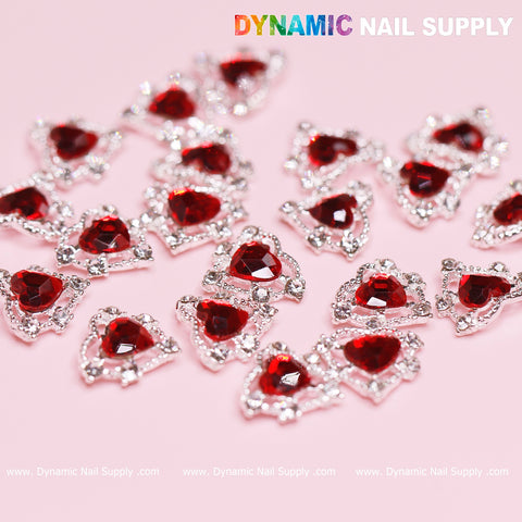A set of 20 sparkling red 3D heart rhinestone charms with silver claw bases scattered on a light pink surface. The top right corner showcases the vibrant, bold text "Dynamic Nail Supply," making it ideal for your next stunning nail art design.