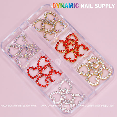 A clear container with six compartments elegantly displays the Dynamic Nail Supply Rhinestones Heart Charm for Nails Art Design, featuring 30 pieces in gold, red, and silver. These charms are arranged across two compartments each and are beautifully set against a soft pink background with Dynamic Nail Supply printed at the top.
