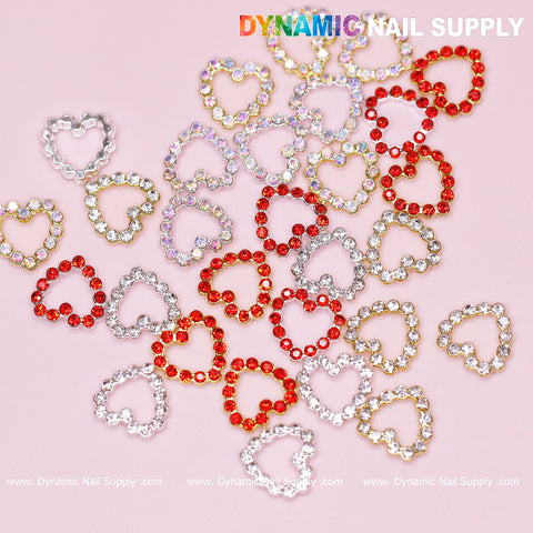 Heart-shaped nail charms with rhinestone borders add a sparkling touch to a Nails Art Design in red, gold, and silver on a pink background. The bold white letters of "Dynamic Nail Supply" are prominently displayed at the top and bottom, highlighting the appeal of the 30 pcs Rhinestones Heart Charm for Nails Art Design (Rhinestones Border Edge, Open Heart).
