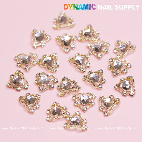 Introducing the "20 pcs Luxury Heart Charm for Valentine Nails Design" from Dynamic Nail Supply. These exquisite nail accents showcase clear gems with gold trim, beautifully set against a light pink background. Each reflective gem is adorned with a border of small rhinestones, making them an ideal choice for a stunning Valentine nails design.
