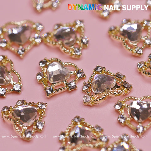 Valentine nails featuring intricate designs of gold-bordered heart and triangle shapes, embellished with sparkling clear gems on a pink background, offer a luxurious touch with their rhinestone accents. The Dynamic Nail Supply logo is prominently displayed at the top of the image.