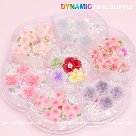 A round plastic container featuring eight compartments presents a collection of vibrant nail art decorations, including elements from the Valentine Nails Art Design such as pink and 3D 5D rose flower charm shapes. The addition of tiny white pearls adds an elegant touch. The text "Dynamic Nail Supply" is elegantly displayed in the top right corner.