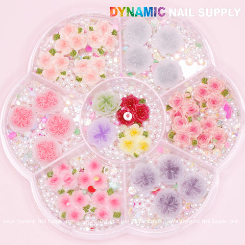 A plastic circular tray contains 40 pieces of white and pink 3D rose flower charms complete with pearls and accessories for Valentine nails. Each compartment holds different color variations, including enchanting pinks and subtle whites, along with intricate bead and sequin embellishments. The brand name, Dynamic Nail Supply, is prominently displayed at the top. Perfect for Valentine nail art designs!