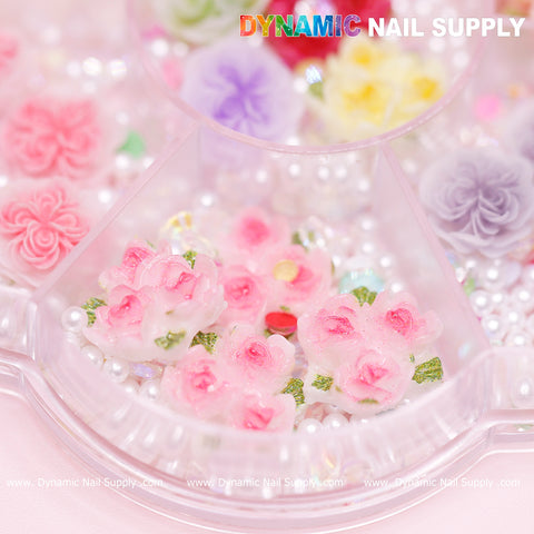 The image showcases a clear container filled with 40 pieces of white and pink 3D/5D rose flower charms, accented by small white pearls and vibrant floral designs, making it an ideal choice for Valentine’s nail art. The top features the Dynamic Nail Supply brand name nestled amongst gently colored flowers.