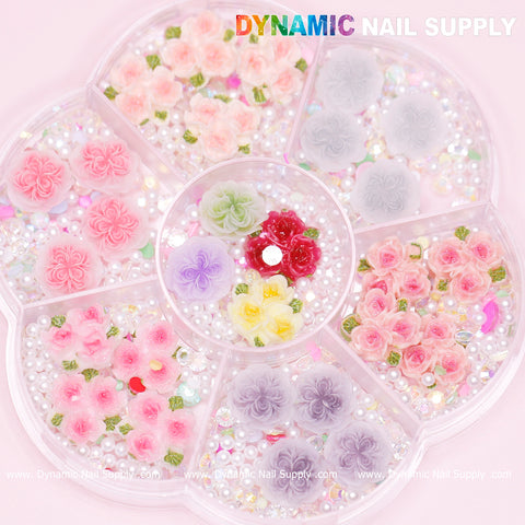 Close-up of a segmented, circular acrylic container from Dynamic Nail Supply showcasing the "40 pcs White and Pink 3D 5D Rose Flower Charm with pearls Accessories for Valentine Nails Art Design." Each section offers colorful charms in shades of pink, purple, red, and white—perfect for crafting stunning Valentine nail art designs against a light pink backdrop.