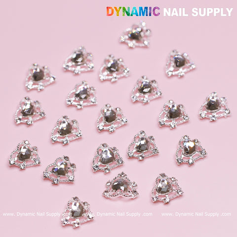 A collection of 20 sparkling silver heart-shaped rhinestone charms from Dynamic Nail Supply, ideal for a Valentine nails design, showcased on a pink surface. Each heart charm is adorned with a central crystal and surrounded by smaller stones. The background includes the text "Dynamic Nail Supply" in multiple locations.