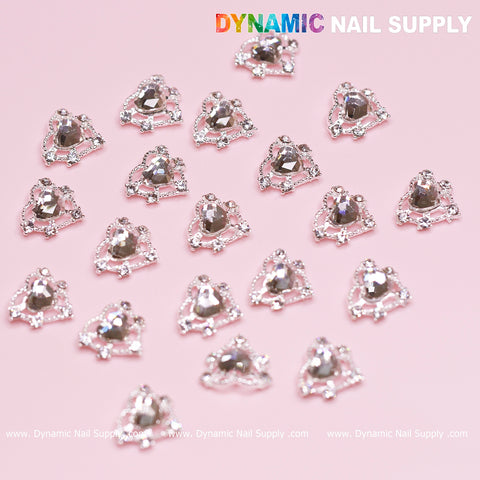 A pink background displays several silver heart rhinestone nail art charms, elegantly arranged in rows, making them perfect for a Valentine nails design. In the top right corner, the colorful text "Dynamic Nail Supply" is prominently featured, with "www.DynamicNailSupply.com" repeated at the bottom.