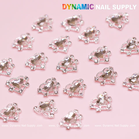 A set of 20 silver heart charms, designed as crystal heart rhinestones perfect for a Valentine Nails Design, glistens on a pink background. The silver edges capture the light in sparkling rows, exuding charm. In the upper right corner, the text 'Dynamic Nail Supply' is prominently displayed.