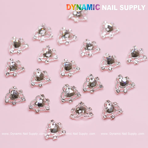 A set of 20 heart-shaped, silver-colored crystal rhinestone nail decorations elegantly displayed on a light pink background. Each features a large central heart crystal accentuated by smaller sparkling stones, ideal for a Valentine nails design. The text Dynamic Nail Supply is located at the top right corner.