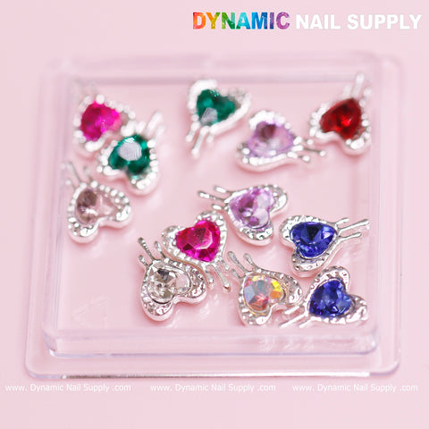 Dynamic Nail Supply's "12 pcs Heart Charm with silver edge (Bleeding/Dripping) for Valentine Nails Design" offers a stunning collection of heart-shaped rhinestones. Perfect for Valentine nail designs, these heart charms come in various colors like pink, green, and blue and are adorned with silver edges and tiny clear crystals. They're neatly displayed on a transparent stand featuring the Dynamic Nail Supply logo at the top.