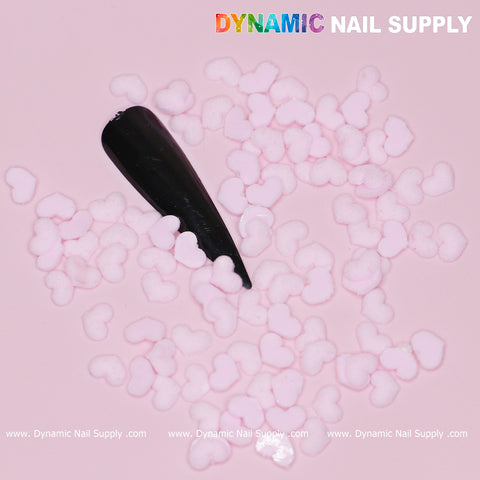 A black nail tip features small, pastel light pink heart-shaped decorations set against a light pink background, making it ideal for Valentine nails. The top right displays the brand name Dynamic Nail Supply, while the product name "90 pcs Pastel Light Pink Heart Charm for Valentine Nails Design" is elegantly repeated along the bottom edge.