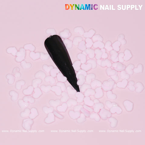 A swatch of black nail polish on a light pink background is adorned with small, pastel light pink heart charms, reminiscent of the 90 pcs Pastel Light Pink Heart Charm for Valentine Nails Design. "Dynamic Nail Supply" is prominently displayed in bold at the top right corner, with branding along the bottom edge.