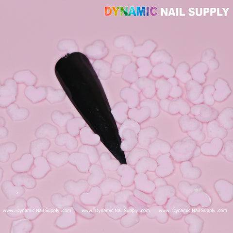 A black nail tip is embellished with small, pastel light pink heart-shaped charms on a pink background. Ideal for Valentine's nail designs, the text Dynamic Nail Supply appears in the top right corner, with www.DynamicNailSupply.com elegantly repeated along the bottom.