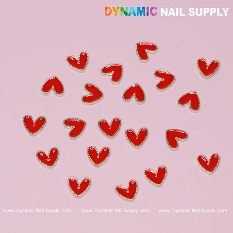 Displayed on the pink surface are heart-shaped nail charms with golden borders, ideal for a Valentine nails design. The image showcases the text "Dynamic Nail Supply" in colorful letters at the top right corner and repeated across the bottom. Product Name: "20 pcs Heart Charm with Golden Borders for Valentine Nails Design" by Dynamic Nail Supply.