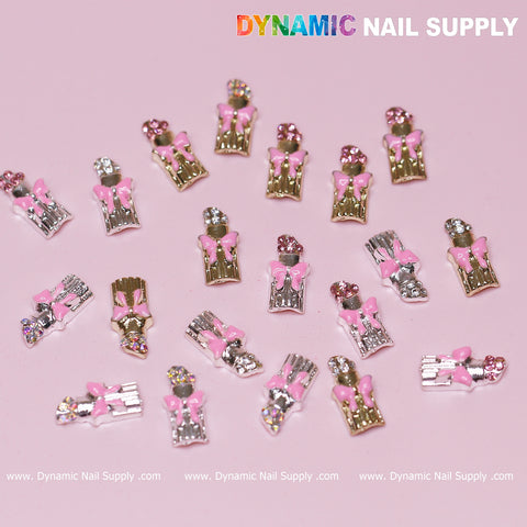 A collection of lipstick charms adorned with pink bows, designed for Valentine's nail art, set against a pink backdrop. These standout pieces resemble small gift boxes embellished with rhinestones. The brand name "Dynamic Nail Supply" is prominently displayed in vibrant white lettering at the top right corner.