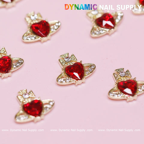 The 12-piece set of Vivienne Westwood Vintage Red Heart Charms for nail art, from Dynamic Nail Supply, features gold heart-shaped designs with vibrant red centers and is surrounded by silver rhinestones. These ornate charms rest against a soft pink background, while the brand name Dynamic Nail Supply is prominently displayed at the top and bottom in colorful text.