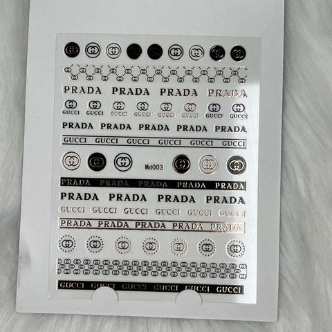 A sheet of fashion-themed nail stickers from Dynamic Nail Supply, featuring their Logo Sticker for nails art design - Md003 in Rose Gold, is elegantly displayed on a white, textured surface. These peel stickers showcase chic logos and brand elements in eye-catching rose gold. Circular and rectangular designs in various sizes are neatly arranged in rows, perfect for elevating your nails.