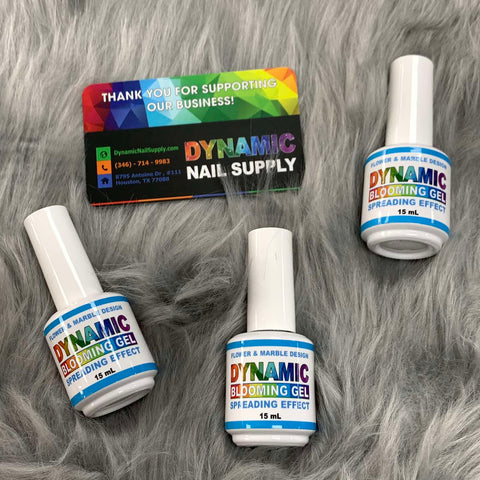 Three bottles of Dynamic Blooming Gel, each 15 mL with Marble Spreading Effect designed for creating flower and marble art, are placed on a gray fur-textured surface. A business card for Dynamic Nail Supply, showcasing nail art design and contact information, is positioned above them, accompanied by a vibrant thank-you message.