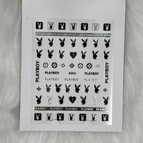 A sleek sheet from Dynamic Nail Supply, featuring the Logo Sticker for nails art design -Md006 in Silver, displays the iconic Playboy bunny logo, the word PLAYBOY, hearts, and small circular designs. Simply peel these stickers from their white background to achieve stylishly neat nail art.