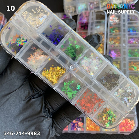 A close-up of a gloved hand holding a clear plastic organizer box showcases the NAIL DESIGN GLITTERs from Dynamic Nail Supply, featuring assorted star-shaped nail art sequins in various colors that add a sparkling touch. The background displays additional containers filled with nail design supplies, accompanied by text that reads "Dynamic Nail Supply" and includes the phone number 346-714-9983.