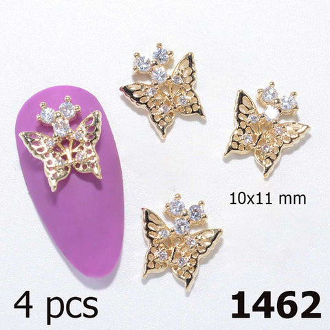 The display features four gold 3D Butterfly Charms for Nails Art Design from Dynamic Nail Supply, highlighted with rhinestone accents. One charm is elegantly showcased on a purple nail tip, emphasizing its intricate cut-out patterns. Measuring 10x11 mm, these charms provide a sparkling finish to any nail art design. Text displays "4 pcs" and "1462" in black font.