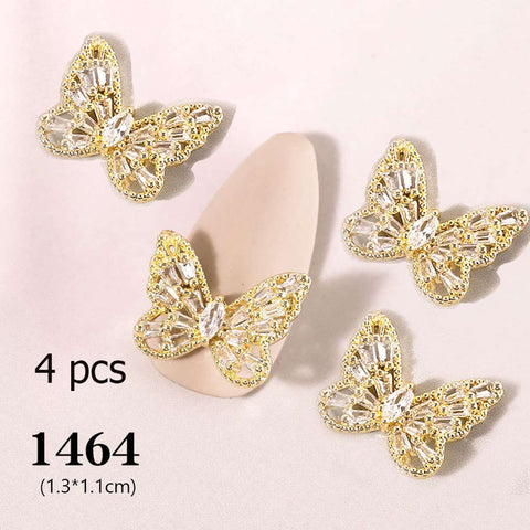 Four 3D butterfly charms from Dynamic Nail Supply are showcased on a soft pink surface. Featuring gold and crystal accents with intricately faceted transparent stones forming the wings, they are ideal for nail art design. The accompanying text reads "4 pcs 3D Butterfly Charm (code 1464)" to indicate the quantity and size of these delicate embellishments, measuring 1.3 cm by 1.1 cm each.