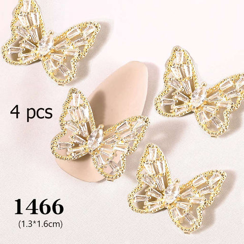 Four gold and crystal butterfly charms are elegantly showcased on a light surface. These nail art designs feature intricate clear stones and gold outlines. A beige, almond-shaped background is partially visible. The text reads "4 pcs 3D Butterfly Charm for Nails Art Design (code 1466)," ideal from Dynamic Nail Supply.