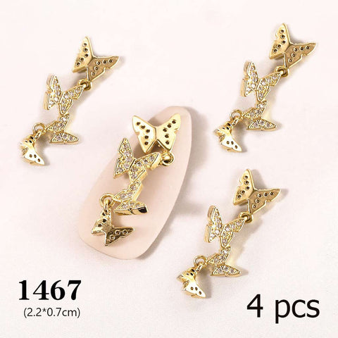 Displayed on a white surface, these gold-toned butterfly charms from Dynamic Nail Supply feature small, sparkling stones. Three smaller butterflies dangle intricately from a larger one to enhance your nail art designs. The text at the bottom reads: 1467 (2.2*0.7cm) and 4 pcs, referring to the 4-piece set of 3D Butterfly Charms for Nails Art Design.