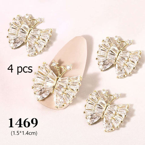 Displayed are four butterfly-shaped rhinestone charms for nail art, each featuring a gold outline and sparkling crystal wings. The text "4 pcs" appears on the left, while "1469 (1.5*1.4cm)" is positioned at the bottom. A pale pink oval background adds a delicate touch, courtesy of Dynamic Nail Supply's 4 pcs 3D Butterfly Charm for Nails Art Design (code 1469).