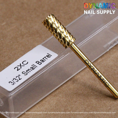On a light brown surface sits an elegant gold, cylindrical nail drill bit from Dynamic Nail Supply. Made of tungsten carbide, the 2XC Double Extra Coarse Drill Bit - Small Barrel Carbide is ideal for removing gel or acrylic nails. It comes with a transparent case labeled "2XC 3/32 Small Barrel.