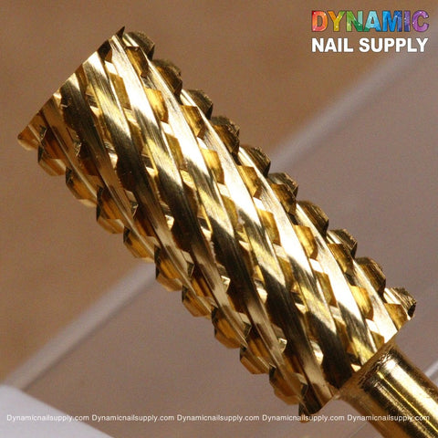 A close-up showcases the 2XC Double Extra Coarse Drill Bit - Small Barrel Carbide, which features a gold-toned, cylindrical shape with a textured, spiral design. Made from tungsten carbide, this drill bit is ideal for removing gel or acrylic nails. The background displays a blurred surface, while the top right corner highlights Dynamic Nail Supply in rainbow colors.