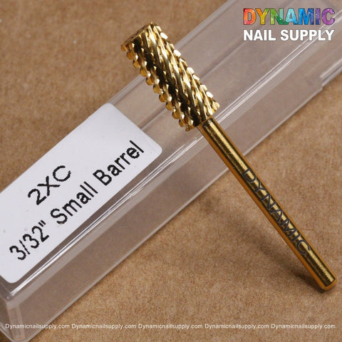 A gold small barrel carbide drill bit, perfect for gel or acrylic nail removal and featuring a textured cylindrical head, rests diagonally on a brown surface. Nearby is a transparent case labeled "2XC Double Extra Coarse Drill Bit." In the top right corner, "Dynamic Nail Supply" is displayed in colorful letters with the website URL beneath it.