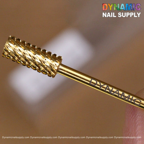 Close-up image of a gold-colored 2XC Double Extra Coarse Drill Bit with a textured cylindrical head. The handle is engraved with "DYNAMIC." Perfect for gel or acrylic nails removal, this tungsten carbide bit ensures precision. The Dynamic Nail Supply brand name appears in colorful text at the top right corner.