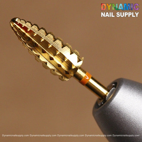 A close-up shows the 2XC Typhoon Bit, a gold conical drill bit with a textured spiral design, ideal for removing acrylic and gel polish. It's attached to a metallic gray nail drill. The warm beige background displays the Dynamic Nail Supply logo in colorful letters, with the website URL repeated across the bottom.