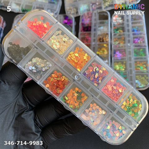 A gloved hand holds a rectangular container with multiple compartments, each filled with colorful, shimmering sequins and glitter from the NAIL DESIGN GLITTER 5 collection. The dazzling array includes hues ranging from reds and oranges to greens and yellows. "Dynamic Nail Supply" is displayed alongside a phone number in white text on the image.