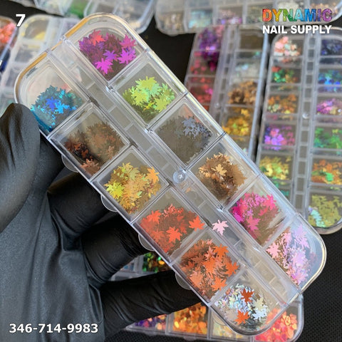 A black-gloved hand holds a transparent plastic box filled with vibrant, maple leaf-shaped nail art pieces and shiny glitter. The background displays more similar organizers. Text reads Dynamic Nail Supply, showcasing their NAIL DESIGN GLITTER 7, along with a phone number and the number 7 in the upper left corner.
