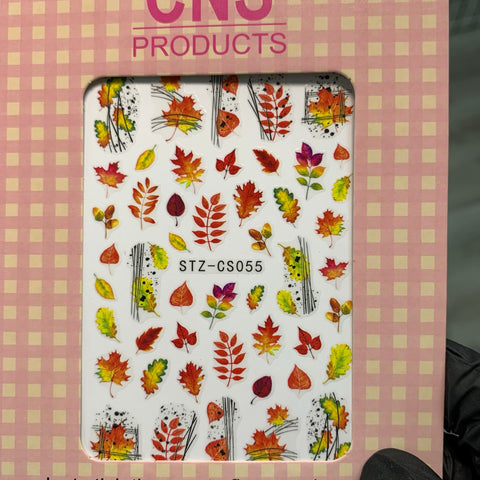 Introducing the FALL Nail Designs Stickers for Fall Season 2021 by Dynamic Nail Supply, featuring a decorative sheet of vibrant autumn leaf stickers perfect for fall nail art. These stickers display stunning shades of orange, red, yellow, and green with leaves artistically arranged alongside abstract black lines. The STZ-CS055 package is accented with a pink and white checkered border and prominently displays CNS Products at the top.