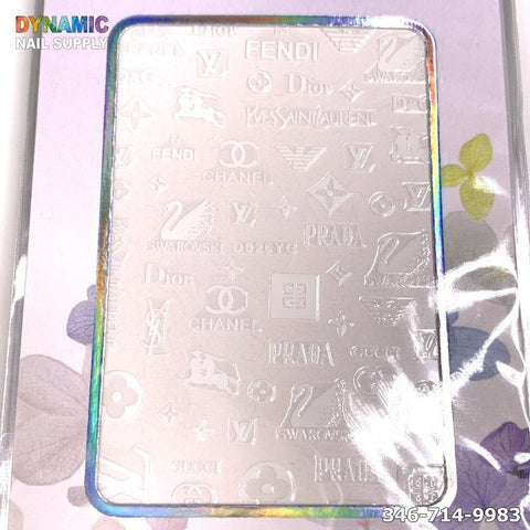 A close-up of a metallic nail stamping plate showcases luxury brand logos such as Chanel, Prada, and Dior. The plate is accented by a shiny, iridescent border and bears the code D026YG along with the Dynamic Nail Supply logo in the corners. A floral design enriches the background for added elegance.