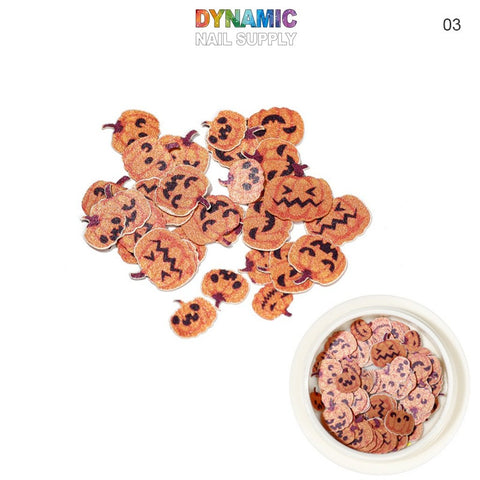 A set of small, decorative Halloween Sequins for Nail Art Design featuring jack-o-lantern shapes with diverse facial expressions is spread across a white background. Perfect for Halloween-themed nail art, these festive pieces are created by Dynamic Nail Supply and are identified with the number 03 in the corner.