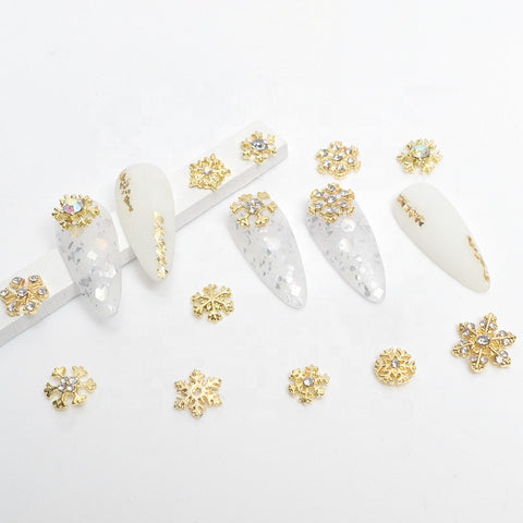 Displayed is a set of decorative nail art pieces by Dynamic Nail Supply, featuring long, almond-shaped nails with matte white and translucent finishes. These 24 pcs are adorned with gold and pearl accents, including intricate snowflake and floral embellishments. The background is white.