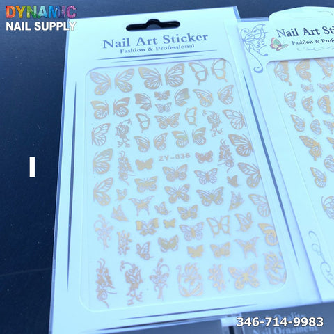 The nail art sticker packaging is showcased up close, with a clear plastic cover displaying an array of Holographic Metallic Butterfly Stickers for Nail Art Design, featuring various metallic gold foil designs and flower patterns. The brand name Dynamic Nail Supply is prominently visible in the top left corner, alongside a contact number, 346-714-9983, located in the bottom right.