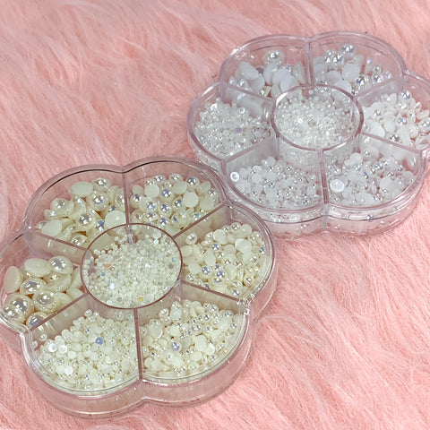 Two flower-shaped containers from Dynamic Nail Supply feature a collection of small beads, including their White Half Pearl Beads for nail art design. These segmented containers offer an assortment of beads in diverse sizes and finishes, showcasing shades of white, cream, and translucent hues. Elegantly displayed on a soft pink faux fur surface, they make a perfect choice for enhancing nail art designs.