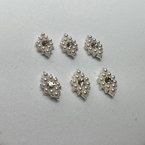 Six rhombus-shaped charms from Dynamic Nail Supply feature clusters of pearls and sparkling clear gems, arranged evenly on a plain white background. The pearls and gems are set on a silvery base, creating an elegant nail art design with an intricate pattern.