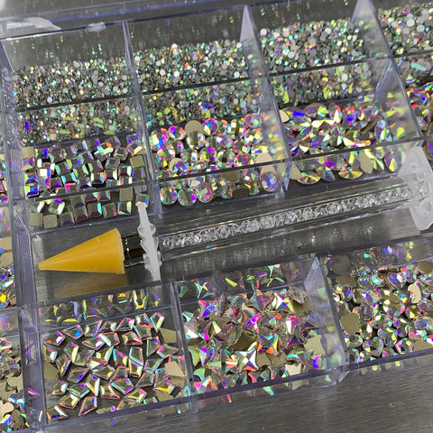 The Dynamic Nail Supply [AB Iridescent gold-back] Rhinestones set boasts a selection of iridescent rhinestones in various shapes, including 14 large designs and 6 round ones. At the center is a wax-tipped tool featuring a rhinestone-filled handle, ideal for picking up and applying these sparkling gems.