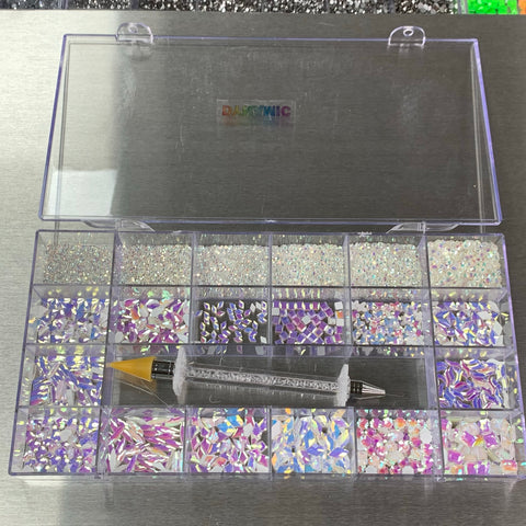 A White Pearl Iridescent Rhinestones set from Dynamic Nail Supply showcases 20 compartments filled with iridescent nail art charms, featuring 14 big shapes and 6 round shapes. Each compartment is packed with an assortment of colorful and shiny decorations. A dual-ended rhinestone picker tool with a yellow tip is resting on top.