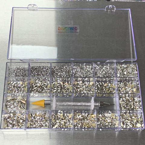 A clear plastic organizer from Dynamic Nail Supply showcases the [Platinum gold-back] Rhinestones set, featuring 14 big shapes and 6 round shapes with shimmering metallic finishes. A rhinestone picker with a yellow tip is centrally placed. The lid, slightly open, reveals a subtle DAITWIC label against the shiny silver surface—perfect for nail supply enthusiasts.
