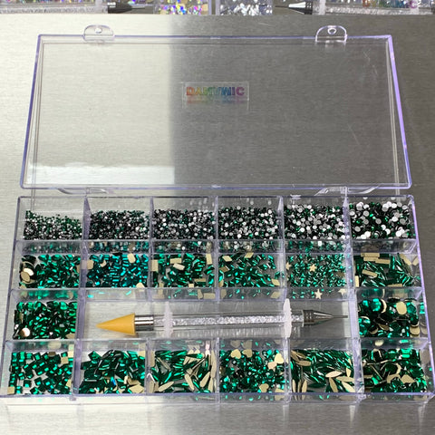 Dynamic Nail Supply's [Emerald Green] Rhinestones Set comes in a 20-compartment box featuring an assortment of green, silver, and black rhinestones that are ideal for nail supplies. Each section stores unique gems for a neat arrangement. Additionally, an emerald green rhinestone picker tool with a yellow tip and crystal-filled handle complements the metallic surface beautifully.