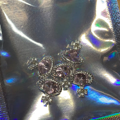 Close-up of sparkling charms designed for nail art, featuring pink rhinestones set in a gleaming silver base from Dynamic Nail Supply. These "5 pcs Planet Charm for Nails" are adorned with clear crystals along the edges and arranged on a reflective, iridescent silver surface, creating a captivating, colorful shimmer that would inspire any nail art designer.